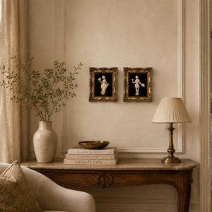May include: An interior shot featuring a decorative console table with a lamp, books, and a vase with greenery. Two framed artworks with gold frames hang on the wall. The room has a neutral color palette with a classic, elegant aesthetic.