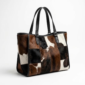 May include: A patchwork tote bag with a cowhide design. The bag features a mix of brown, black, and white patches. It has black leather handles and trim, and is designed for carrying items.