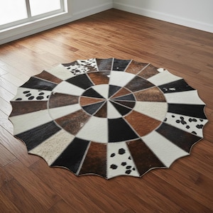 May include: A circular cowhide rug with a patchwork design. The rug features segments of brown, black, white, and spotted cowhide arranged in a circular pattern. It is placed on a wooden floor.