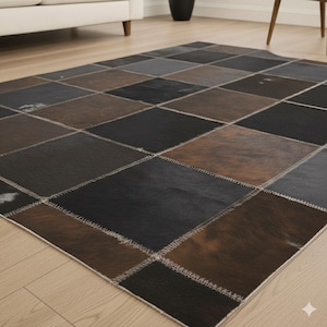 Könnte beinhalten: Ein rechteckiger Patchwork-Teppich mit geometrischem Muster. Der Teppich besteht aus Quadraten in Schwarz-, Braun- und Grautönen, die mit hellem Faden zusammengenäht sind. Der Teppich liegt auf einem hellen Holzboden. Das Design des Teppichs verleiht einen rustikalen Charme.
