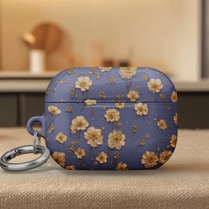 May include: A blue AirPod case with a floral pattern. The case is covered in a repeating pattern of beige flowers and stems. A silver-colored metal ring is attached to the side of the case.