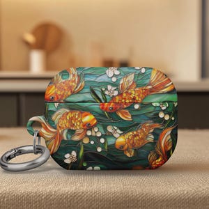 May include: A decorative case for wireless earbuds featuring a colorful koi fish design. The case has a teal background with orange and yellow fish, white flowers, and a silver carabiner clip.