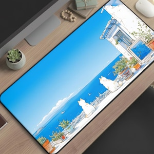 May include: A rectangular mouse pad featuring a coastal scene with white cats, blue sky, and ocean view. The design includes a building with potted plants and a window. The pad is on a wooden desk with other office supplies.