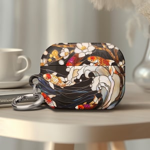May include: A black and gold AirPod case featuring a koi fish design. The case has a silver carabiner clip. The design includes orange, red, and white koi fish swimming in a stylized wave pattern with white flowers.