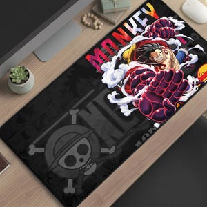 May include: Black rectangular mouse mat featuring a vibrant illustration of a character with red and yellow accents, surrounded by white smoke. The word "MONKEY" is displayed in colourful letters. A skull and crossbones logo is visible.