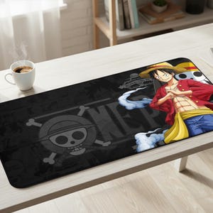 May include: Black rectangular mousepad featuring a graphic of a character from the anime series One Piece. The character is wearing a red shirt, blue pants, and a straw hat. The mousepad also has the One Piece logo.
