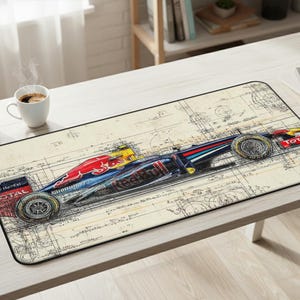 Peut inclure: Tapis de souris rectangulaire avec une illustration détaillée d'une voiture de course de Formule 1 rouge, bleue et jaune, sur fond de plan. Le tapis de souris a une bordure noire et la voiture porte le mot "TOTAL".