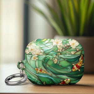 May include: Green and white AirPod case with a koi fish design. The case features a detailed illustration of koi fish swimming in a stylized water scene with white flowers. Includes a silver carabiner clip for attachment.