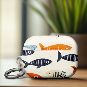 May include: White Airpods case with a colorful fish pattern and a black metal keychain. The case has a white background with orange, blue, and black fish.