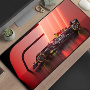 May include: A large rectangular mousepad featuring a Formula 1 race car design. The car is black and red with the word "ORACLE" on the side. The background is a gradient of red and orange.