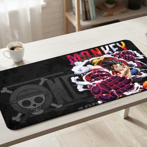 May include: Black rectangular desk mat with a manga character graphic and the word "MONKEY" in rainbow colours. The mat also features a skull and crossbones logo.