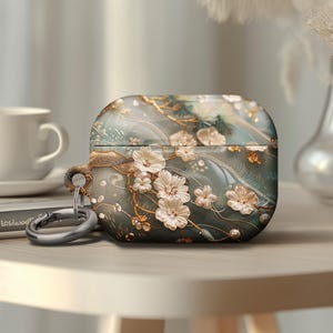 May include: A white and gold floral design Airpods case with a silver keychain. The case has a blue and white marble background.