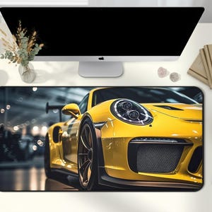 May include: A yellow sports car mousepad featuring a close-up of a bright yellow sports car. The mousepad is rectangular and sits on a white desk, with a computer monitor, books, and other desk accessories.