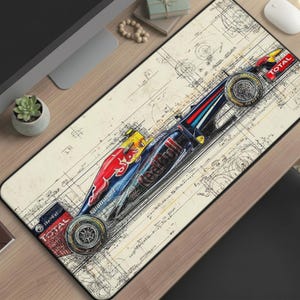 Peut inclure: Tapis de souris rectangulaire avec une illustration détaillée d'une voiture de course Red Bull de Formule 1. La voiture est principalement rouge, bleue et jaune, avec des logos de sponsors. Le fond présente un motif de plan.