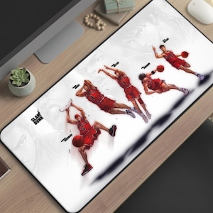 May include: A white rectangular mousepad featuring a basketball player in a red uniform performing a slam dunk. The image shows the player in multiple stages of the dunk, with the word "SLAM DUNK" in the corner.