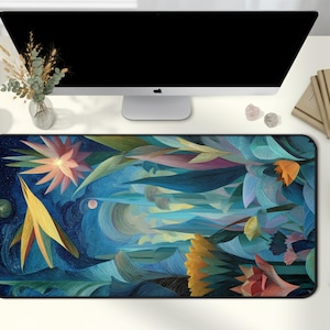 May include: A rectangular desk mat featuring an abstract floral design in blue, yellow, orange, and pink. The mat sits on a white desk, alongside a computer monitor, notebooks, and other desk accessories.