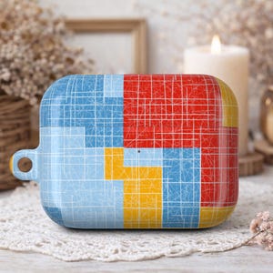 May include: A colorful, geometric patterned case for wireless earbuds. The case features a design of blue, red, and yellow squares with a white grid overlay. It has a small loop for attaching to a keychain or lanyard.