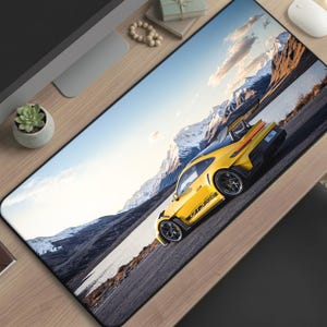 May include: A yellow sports car mousepad featuring a vibrant image of a yellow sports car driving on a mountain road. The car is set against a backdrop of snow-capped mountains and a blue sky. The mousepad is rectangular.