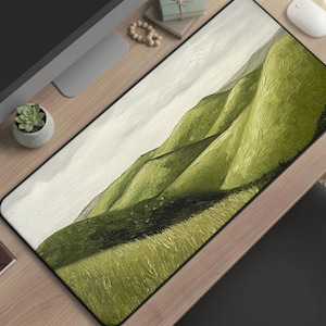 May include: A rectangular desk mat featuring an abstract landscape painting of rolling green hills under a cloudy sky. The mat has a black border and is placed on a wooden desk, alongside a computer monitor, mouse, and other desk accessories.