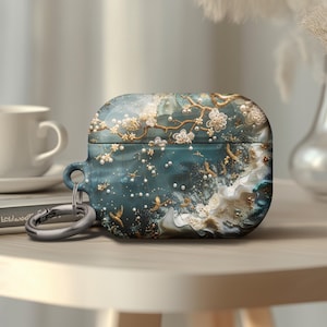 May include: A teal blue Airpods case with a floral design featuring white flowers, gold accents, and a pearl-like texture. The case has a silver metal keychain attached.