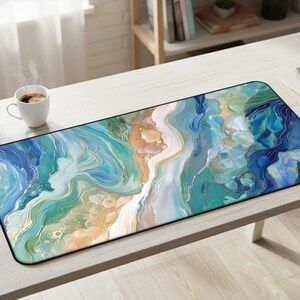 May include: A rectangular desk mat featuring an abstract fluid art design with swirling patterns of teal, navy blue, white, and gold. The surface has a smooth finish with rounded corners and a black edge trim, displaying a marbled aesthetic.