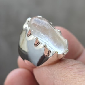 Pode incluir: Um anel de prata com uma grande pedra preciosa oval e translúcida. A pedra preciosa tem uma qualidade leitosa e iridescente. A cravação do anel é em prata polida com um design decorativo em forma de garra.