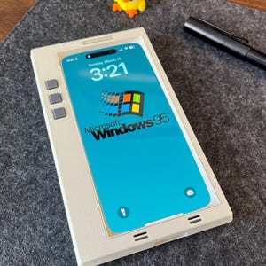 May include: A white phone case with a blue screen displaying the Microsoft Windows 95 logo. The time is 3:21 and the date is Sunday, March 16.