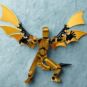 Può includere: Una figura d'azione dorata articolata con dettagli neri e ali stilizzate. La figura è in posa dinamica, accovacciata, con le braccia tese. Le ali sono di un colore oro brillante e una lama nera è attaccata alla gamba.