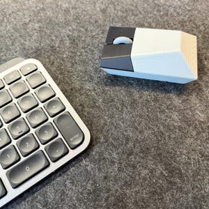 May include: A computer mouse with a light blue and black design sits next to a silver number pad. The mouse has a scroll wheel and a geometric shape. The number pad has black keys with white numbers and symbols.