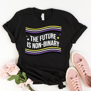 May include: Black t-shirt with a white graphic that says "The Future is Non-Binary" with a yellow, white, purple, and black striped design and stars on either side of the text.
