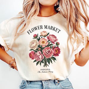 May include: A white t-shirt with a floral design and the text "Flower Market Indiana The Indiana Peony".