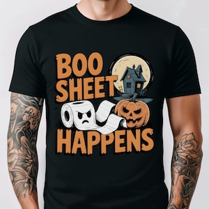 May include: Black t-shirt with a Halloween-themed graphic. The design features the text "BOO SHEET HAPPENS" in orange, along with a cartoon toilet paper roll, a jack-o'-lantern, a haunted house, and a full moon.