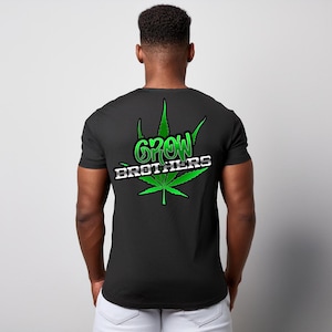 Könnte beinhalten: Schwarzes T-Shirt mit einem grünen Cannabisblatt-Design und den Worten "GROW BROTHERS" in Grün und Weiß. Das Shirt hat kurze Ärmel und einen Rundhalsausschnitt.