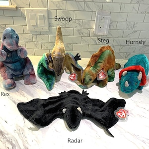 May include: A white ceramic mug with a black handle and the text "But First, Coffee" in a bold, black font. The mug is set against a blurred background, suggesting a cozy setting.