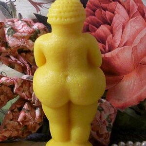 以下が含まれることがあります： 人間のシルエットの形をした黄色の蜜蝋のろうそく。ろうそくは小さな丸い台座の上に立っています。