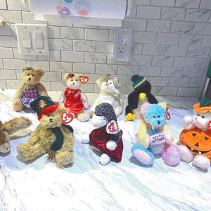 May include: A collection of Ty Beanie Babies plush toys, including bears, a penguin, and a rabbit. The plush toys are in various colors and outfits, some with hats and accessories. One plush toy is holding a sign that says "Happy Birthday".