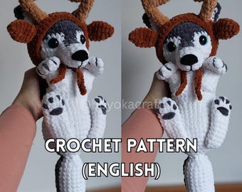 May include: A handmade crochet husky dog wearing a brown reindeer antler hood. The dog is white with gray and black markings, blue eyes, and black paw pads. The text "CROCHET PATTERN (ENGLISH)" is displayed below the dog.