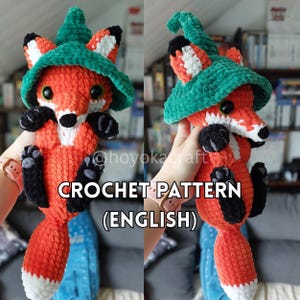 May include: A handmade orange and white crochet fox wearing a green hat. The fox has black paws and a black nose. The text "CROCHET PATTERN (ENGLISH)" is displayed below the fox.