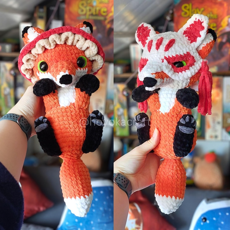 May include: A plush orange fox toy with black paws and a white-tipped tail. The left image shows the fox wearing a ruffled red and beige mushroom-style hat. The right image shows the fox wearing a white and red fox-themed mask with red tassels.