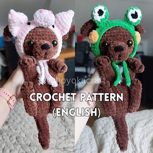 May include: Two brown crochet dog plushies, one wearing a pink pig hat and the other a green frog hat. The plushies have large eyes and are holding their paws up. The text "CROCHET PATTERN (ENGLISH)" is at the bottom.