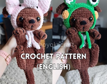 May include: Two brown crochet dog plushies, one wearing a pink pig hat and the other a green frog hat. The plushies have large eyes and are holding their paws up. The text "CROCHET PATTERN (ENGLISH)" is at the bottom.