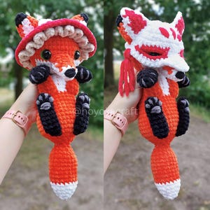 May include: A crochet fox plush toy featuring two interchangeable accessories: a red and white ruffled mushroom-style hat and a white and red fox-themed face mask with red tassels. The fox has orange fur, black paws, and a white-tipped tail.