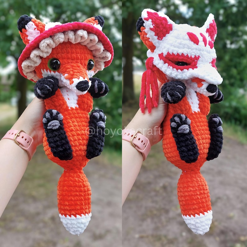 May include: A crochet fox plush toy featuring two interchangeable accessories: a red and white ruffled mushroom-style hat and a white and red fox-themed face mask with red tassels. The fox has orange fur, black paws, and a white-tipped tail.