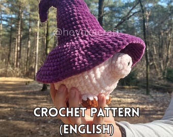 May include: A crocheted mushroom figure with a purple hat and a white and pink body. The text "CROCHET PATTERN (ENGLISH)" is displayed at the bottom of the image. The figure is held in a person's hand.
