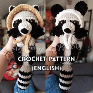 Puede incluir: Un peluche de mapache tejido a crochet, con capucha y bufanda beige. El mapache tiene marcas en blanco y negro, ojos negros grandes y una cola a rayas. El texto "CROCHET PATTERN (ENGLISH)" es visible.