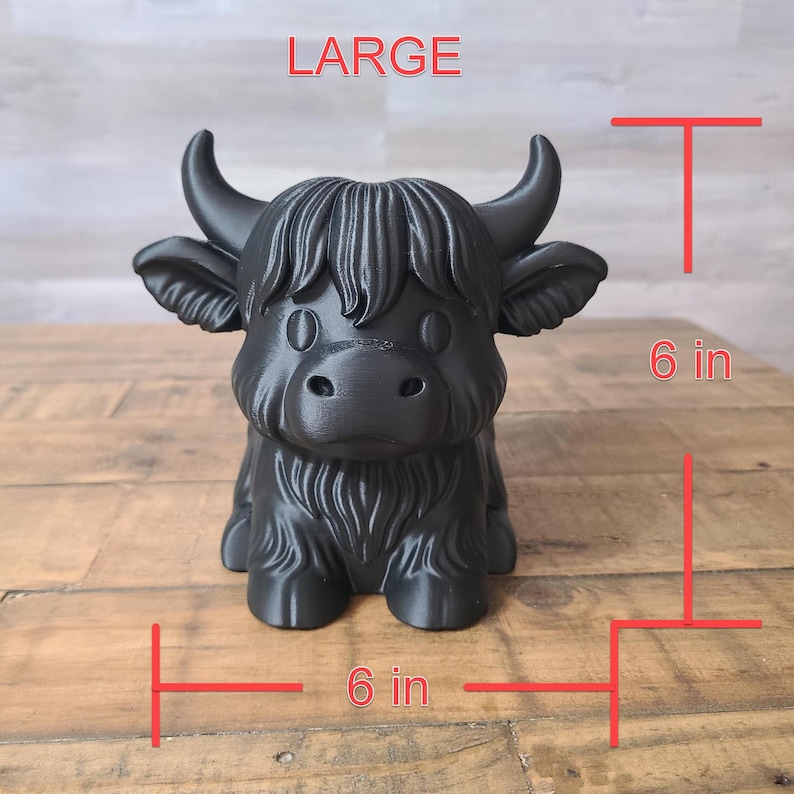 May include: A black Highland cow figurine, labeled "LARGE", is 6 inches (15 cm) tall and 6 inches (15 cm) wide. The cow has a shaggy coat, horns, and large ears. The figurine is sitting on a wooden surface.