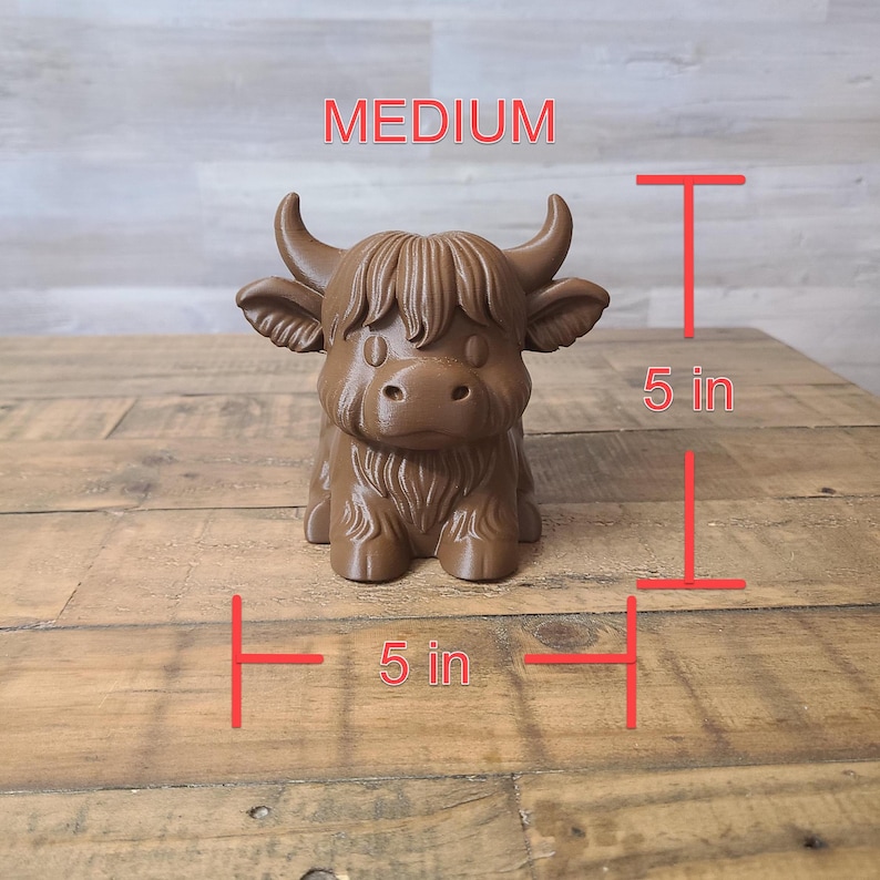 May include: A brown, medium-sized Highland cow figurine, approximately 5 inches tall and 5 inches wide. The figurine has detailed fur and horns, with the word "MEDIUM" above it. The cow is sitting on a wooden surface.