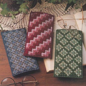 May include: Three handmade eyeglass cases in blue, red, and green, each with a unique stitched design. The blue case has a textured pattern, the red case features a zig-zag pattern, and the green case has a floral design. A pair of glasses rests on one of the cases.