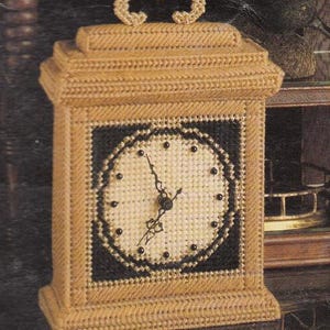 Può includere: Un orologio in arazzo beige e nero con quadrante quadrato e manico decorativo. Il quadrante è bianco sporco con punti neri che segnano le ore e lancette nere. L'orologio ha un'estetica classica e vintage.
