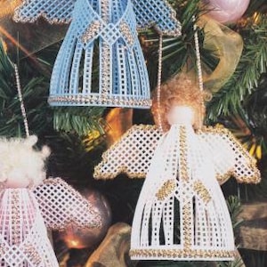 以下が含まれることがあります： 天使の形をした手作りクリスマスオーナメントが3つ。天使は白いプラスチック製のキャンバスで作られており、金色のトリムが施されています。天使はクリスマスツリーに飾られています。